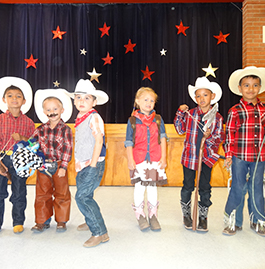 Students in cowboy attire stand in front of a stage